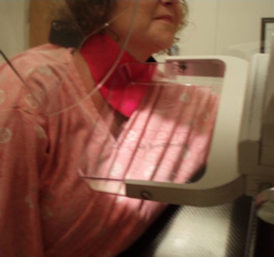 A technologist positioned for a mammogram with the thyroid shield in place. Part of the thyroid shield is underneath the compression paddle and would cause a portion of the breast to be obscured on the mammogram.