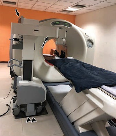 The robotic arm is docked at the side of the PET/CT bed (arrowheads) console for planning (arrow). The dashed arrow shows the working arm of the robot. Image courtesy of AJR.