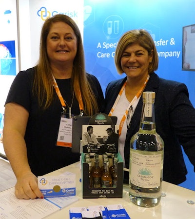 Two women standing with a bottle of tequila