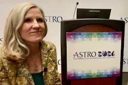 Woman in gold patterned jacket speaking at ASTRO event podium with colorful logo displayed on screen