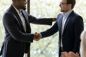 Two businessmen in suits shaking hands in a professional office setting