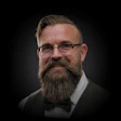 Professional headshot of a bearded man wearing glasses and formal attire with bow tie