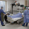 Medical team attending to patient in hospital room with diagnostic imaging equipment and monitoring systems