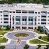 Aerial view of modern multi-story building with circular driveway and manicured landscaping