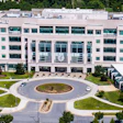 Aerial view of modern multi-story building with circular driveway and manicured landscaping