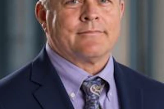 Professional headshot of a middle-aged man wearing a navy blazer and lavender dress shirt with patterned tie