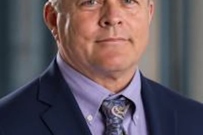 Professional headshot of a middle-aged man wearing a navy blazer and lavender dress shirt with patterned tie