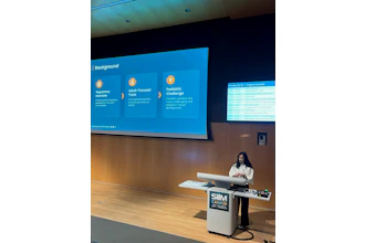 Woman presenting at SIM CAIM26 conference podium with blue program schedule displayed on projection screen