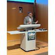Professional speaker at podium with SIIM CAIMI26 conference logo during AI research awards presentation