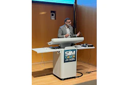 Professional speaker at podium with SIIM CAIMI26 conference logo during AI research awards presentation