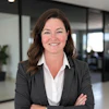 Professional woman in dark blazer and white blouse smiling in modern office setting
