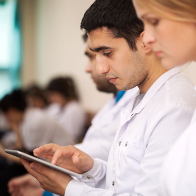 Two professionals reviewing tablet data in a modern office setting with colleagues in background