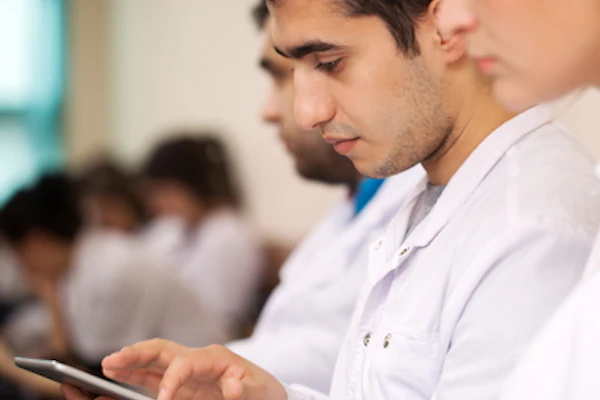 Two professionals reviewing tablet data in a modern office setting with colleagues in background