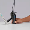 Person holding black handheld dental care device with blue logo and white applicator attachment