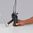 Person holding black handheld dental care device with blue logo and white applicator attachment