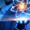Hand holding glowing atom symbol with blue and gold light effects against blurred tech background