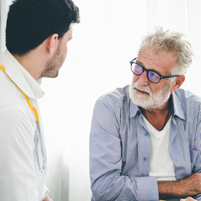 Older man with glasses speaking with younger male healthcare professional in white coat during medical consultation