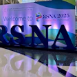 RSNA 2025 welcome sign displaying blue dimensional letters with purple gradient backdrop and event tagline 'Imaging the Individual' in modern lobby setting