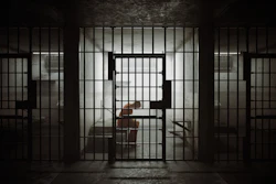 Dimly lit prison cell with barred doors and figure inside, conveying confinement and isolation