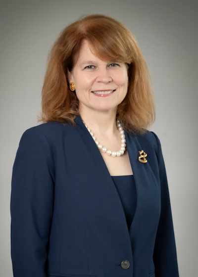 Professional headshot of woman in navy blazer and pearl necklace smiling at camera