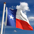 Texas state flag waving on a flagpole against a bright blue sky with white clouds