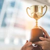 Hands holding a gold trophy cup against a blurred urban cityscape background