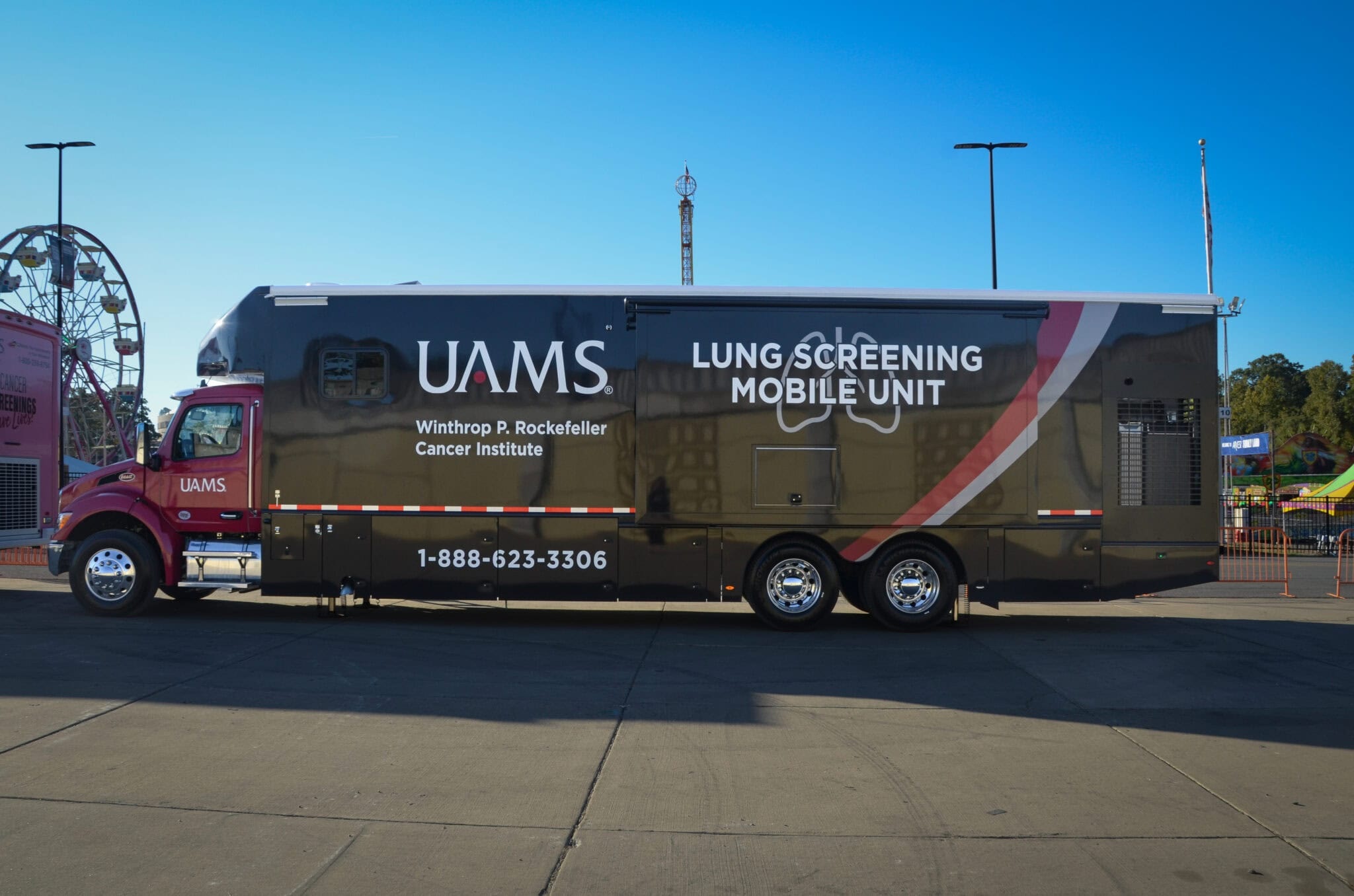 UAMS lung screening mobile unit parked at outdoor venue with Ferris wheel visible in background