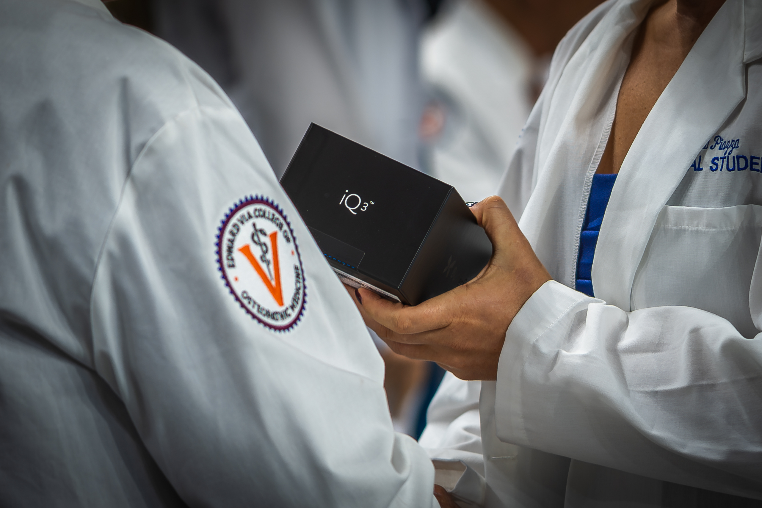 Medical or academic professionals in white lab coats holding a black IQ3 device, with institutional logo visible on garment
