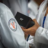 Medical or academic professionals in white lab coats holding a black IQ3 device, with institutional logo visible on garment