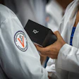 Medical or academic professionals in white lab coats holding a black IQ3 device, with institutional logo visible on garment
